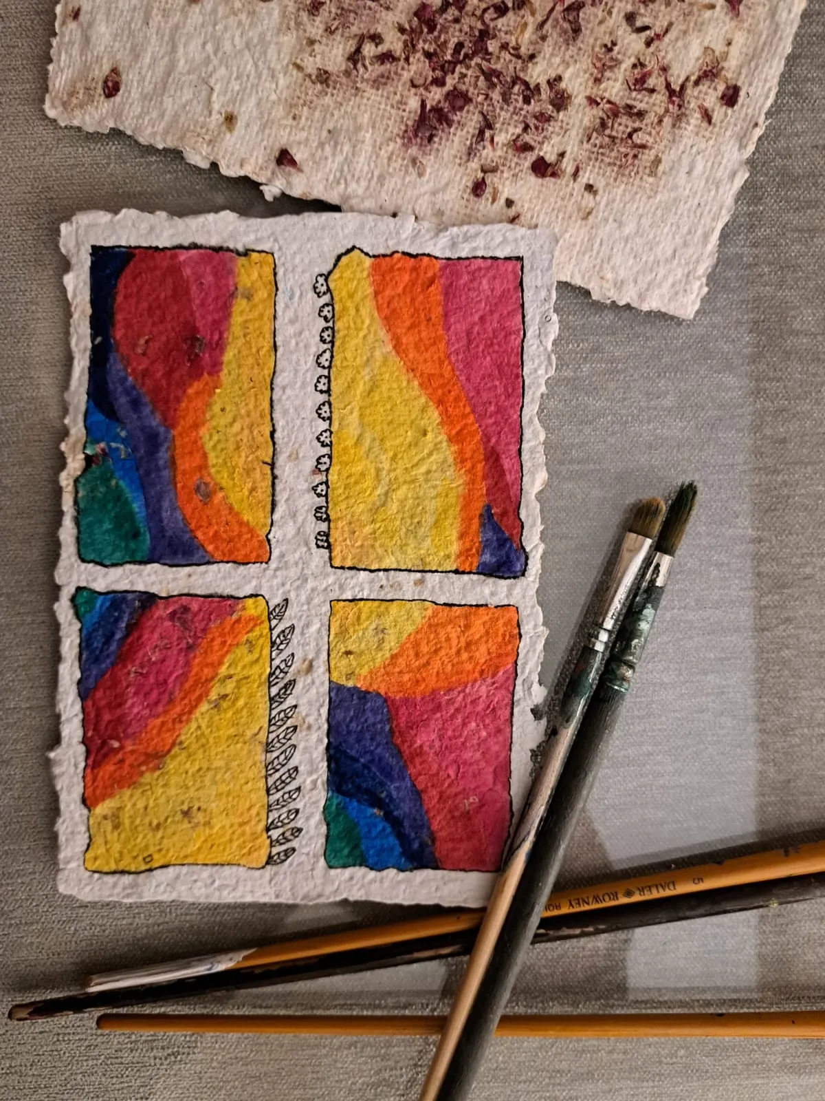 Una ventana de colores pintada sobre una hoja de papel reciclado con pinceles sobre una tela gris de mesa andaluza.